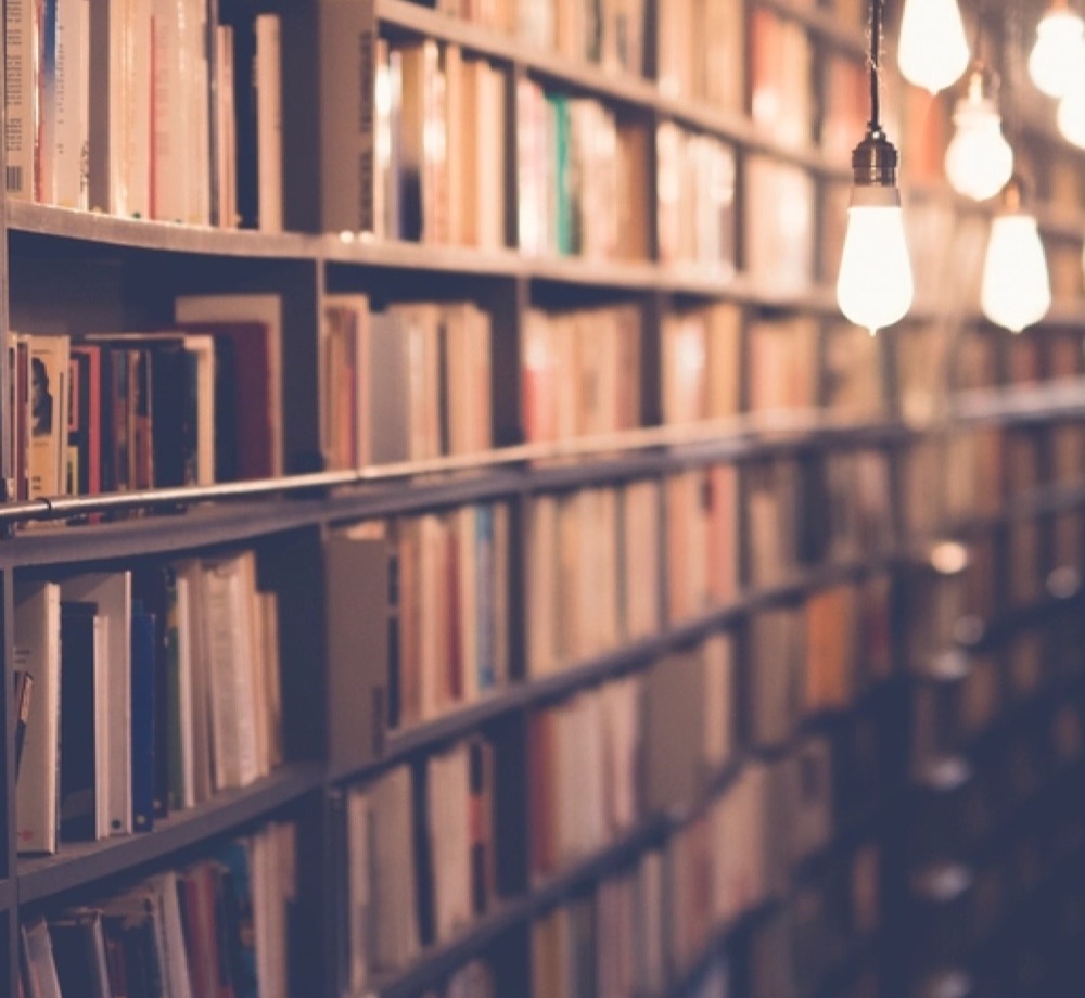 Long shelves of old books under a row of warm hanging bulbs